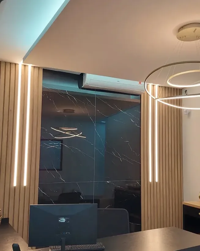 Escritório com ripado amadeirado e fitas de LED verticais emoldurando um painel marmorizado escuro