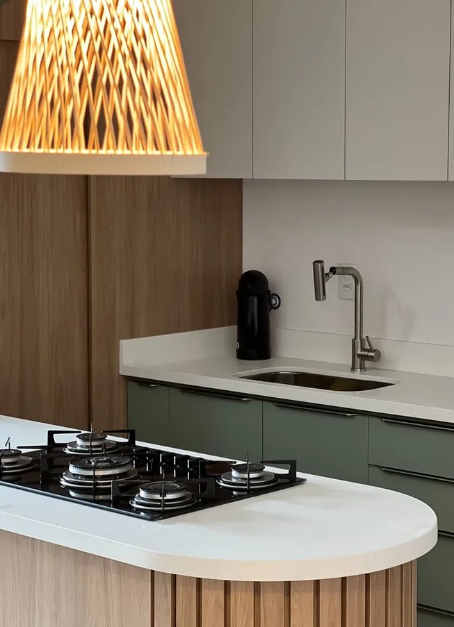 Cozinha com ilha de cantos arredondados revestida em ripado amadeirado, cooktop embutido e armários verde-oliva