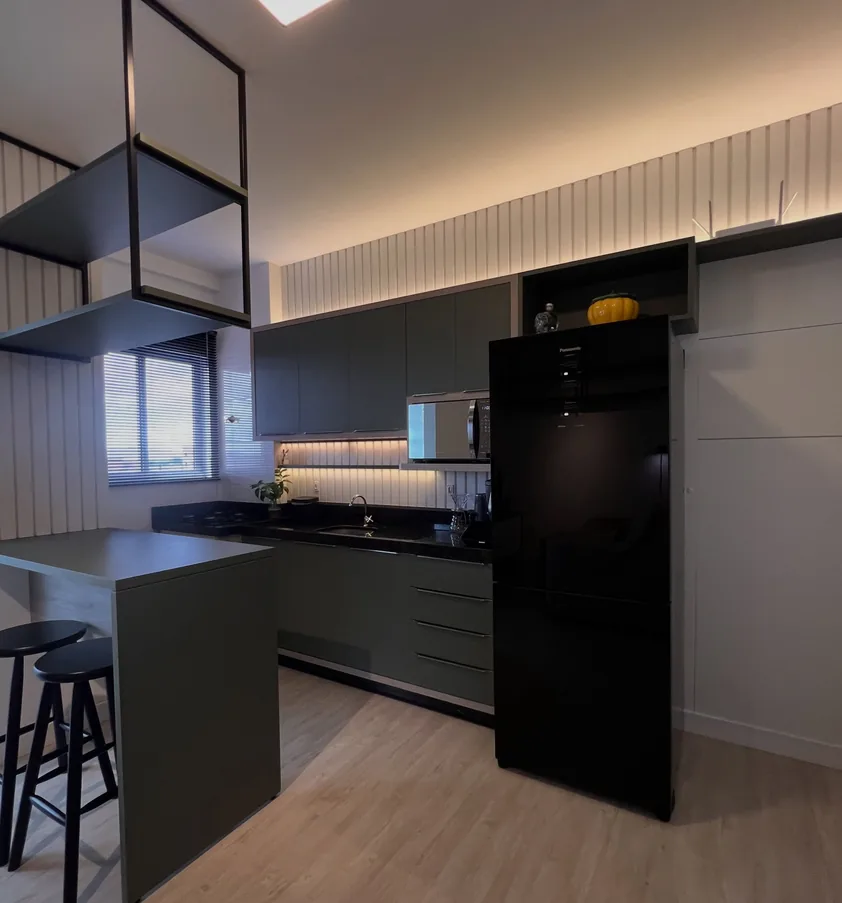 Cozinha com armários verde escuro, balcão para refeições, nicho suspenso metálico e parede ripada com iluminação embutida