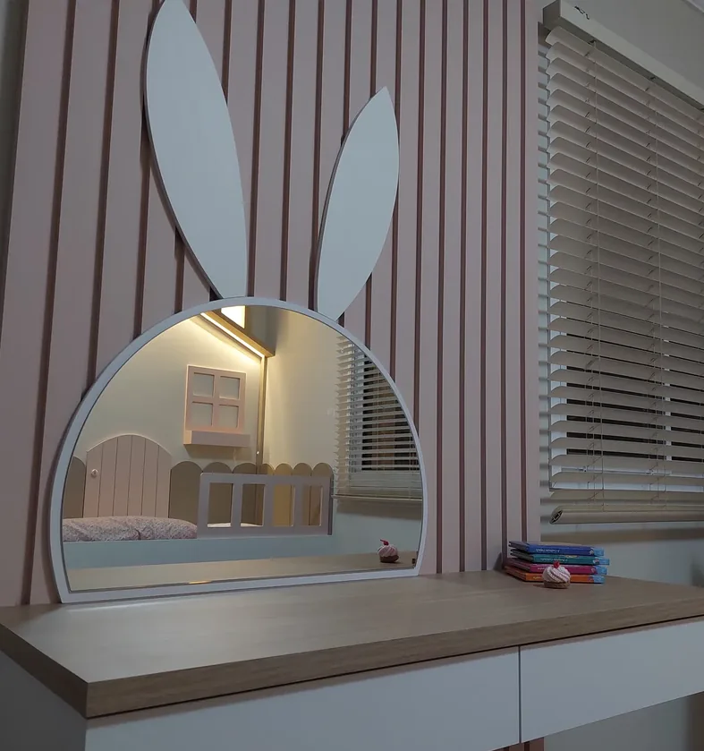 Penteadeira infantil com espelho em formato de coelho sobre painel ripado rosa e tampo amadeirado com gavetas brancas